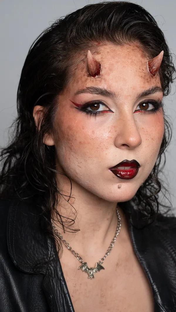 Modelo caracterizada de demonio con dos cuernos pegados en la frente, delineado rojo y negro y labios en degradado oscuro
